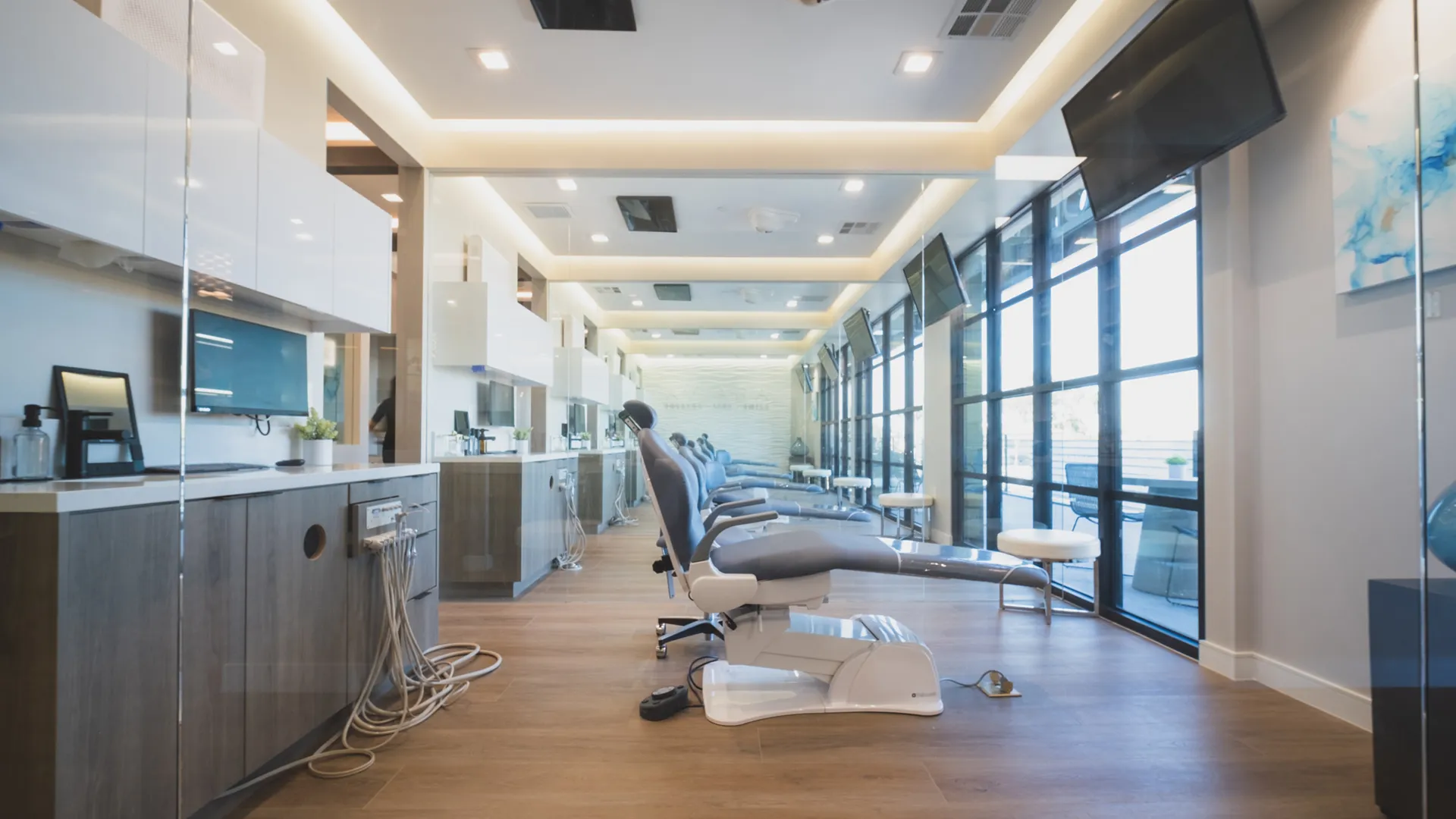 Open dental treatment area at Aviara Centers with multiple operatories, reclining patient chairs, wall-mounted screens, and floor-to-ceiling windows