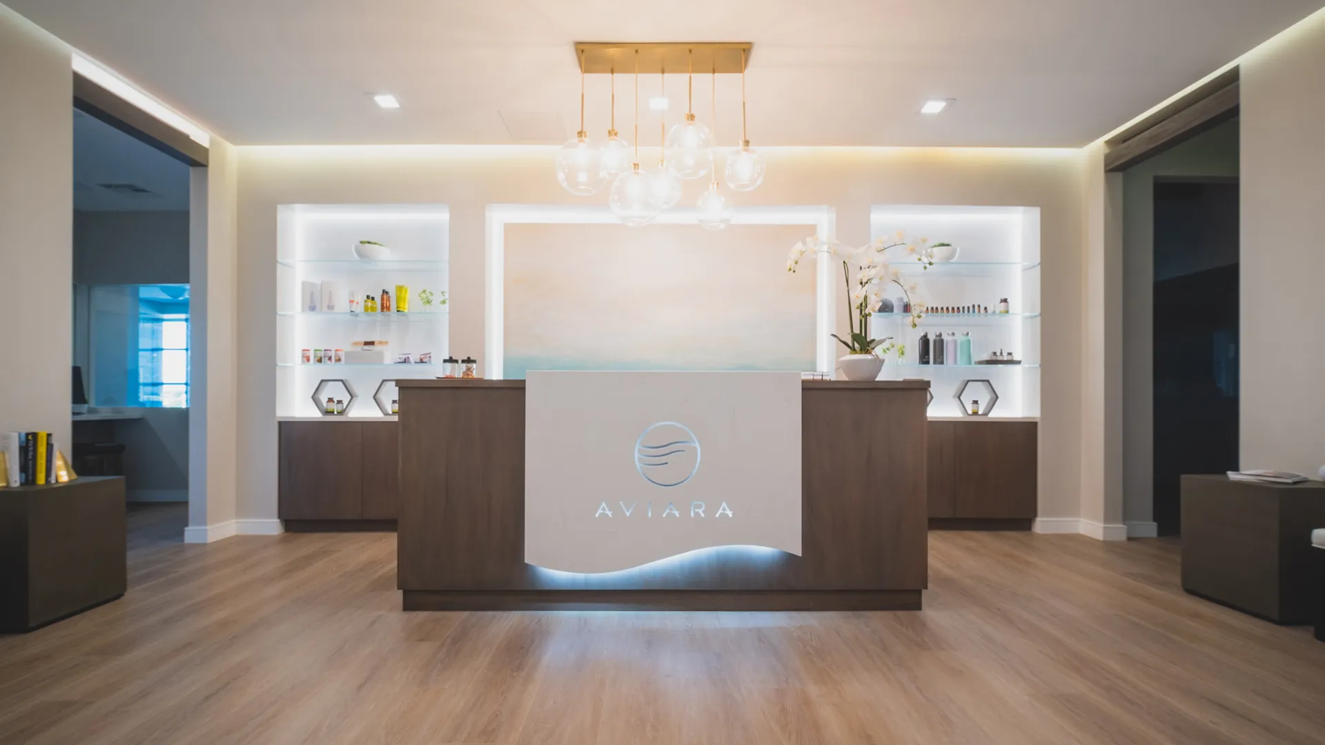 Reception desk at Aviara Centers in Los Alamitos with illuminated Aviara logo, backlit product shelves, and pendant lighting