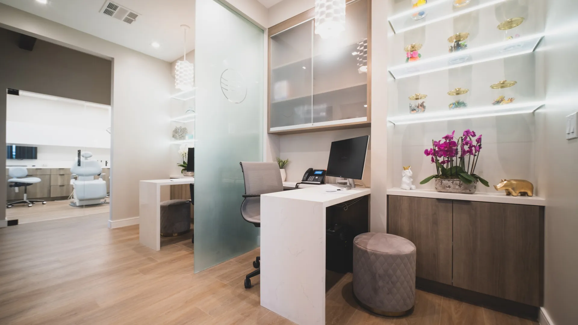 Private consultation workspace at Aviara Centers with desk, frosted glass partition, orchid display, and adjacent treatment room